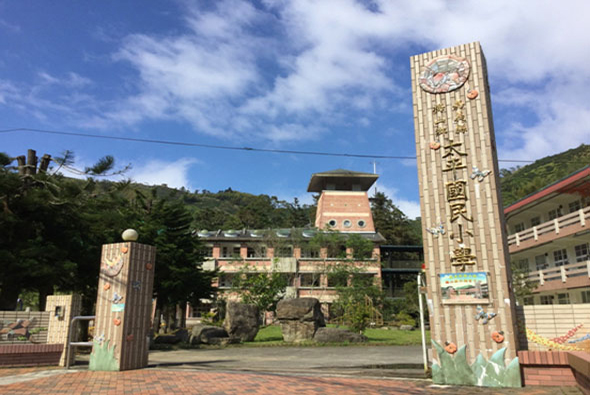 台灣山區廟宇建築，具有傳統中式風格，中央為三層樓塔樓，兩側豎立刻有廟宇名稱的石碑，前方廣場鋪設磚石，四周環繞翠綠山林，藍天白雲。