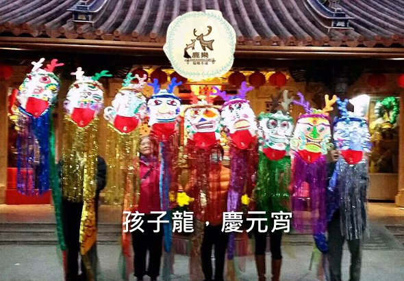 傳統廟宇內懸掛多盞彩色燈籠，燈籠上繪有招財貓圖案，燈籠下方搭配金色流蘇裝飾。廟宇上方掛著圓形白色燈籠，中央印有鹿圖案。下方文字顯示「孩子龍·慶元宵」。