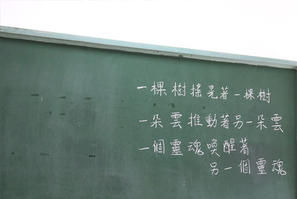 綠色牆面上用白色粉筆書寫的古詩。詩句內容為：一棵樹搖晃著一棵樹，一朵雲推動著另一朵雲，一個靈魂喚醒著另一個靈魂。詩文排列整齊，展現優美的書法筆跡。