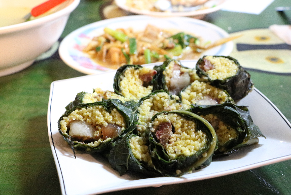 白色盤子裡盛著海苔包裹的糯米卷，內餡為蝦仁和肉類。背景放置多個白色餐盤，盛有炒飯等其他菜肴，擺放在綠色餐桌上的中式餐點。