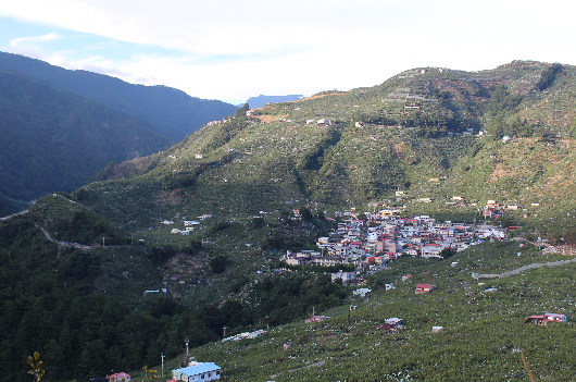 山區村落風景，多彩房屋依山而建，散布在翠綠的山坡上。遠處群山環繞，近處可見藍色建築物，房舍密集分布在不同海拔高度，呈現典型的山地聚落風貌。