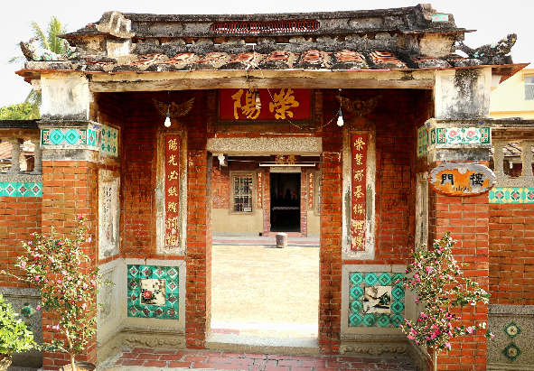 紅磚傳統閩南建築，正門上方懸掛紅色匾額，門框兩側貼有金色對聯。門兩側牆面裝飾著青綠色陶瓷壁畫，屋頂覆蓋著古瓦，邊角長有植物。門前庭院地面鋪設紅磚。