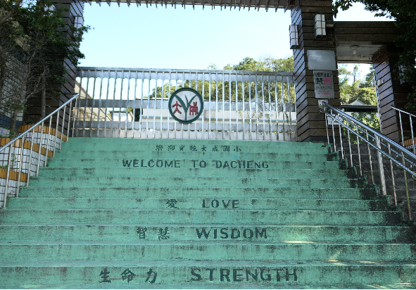 大坑地區階梯上書寫著綠色的歡迎標語，包括「歡迎來到大坑」、「愛」、「智慧」、「力量」等中英文字樣。階梯兩側有石造建築和金屬欄杆，上方有多層天橋跨越。