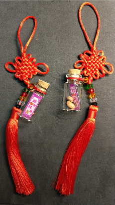 兩個紅色中國結飾品，頂部為編織的紅色結球，下方各掛一個紫色玻璃瓶，內含金色珠飾，底部垂掛紅色流蘇。適合農曆新年或傳統節慶裝飾。