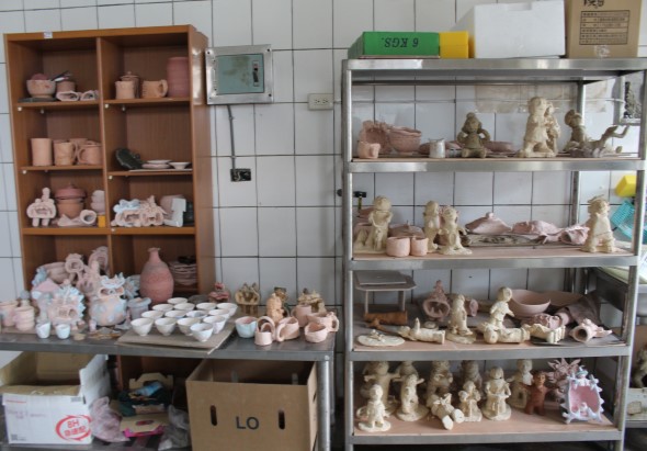 陶藝工作室展示櫃，左側木架放置各式陶製杯盤和裝飾品，右側玻璃櫃展示多層陶塑人像、容器及陶藝作品，展現豐富的陶藝創作成果。