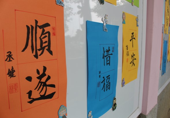 牆面展示多幅書法作品，橙色紙張書寫「順逆」，藍色紙張書寫「惜福」，黃色紙張書寫「平安」等漢字，每幅作品上方均掛有金屬夾具固定，呈現傳統書法藝術展覽風格。
