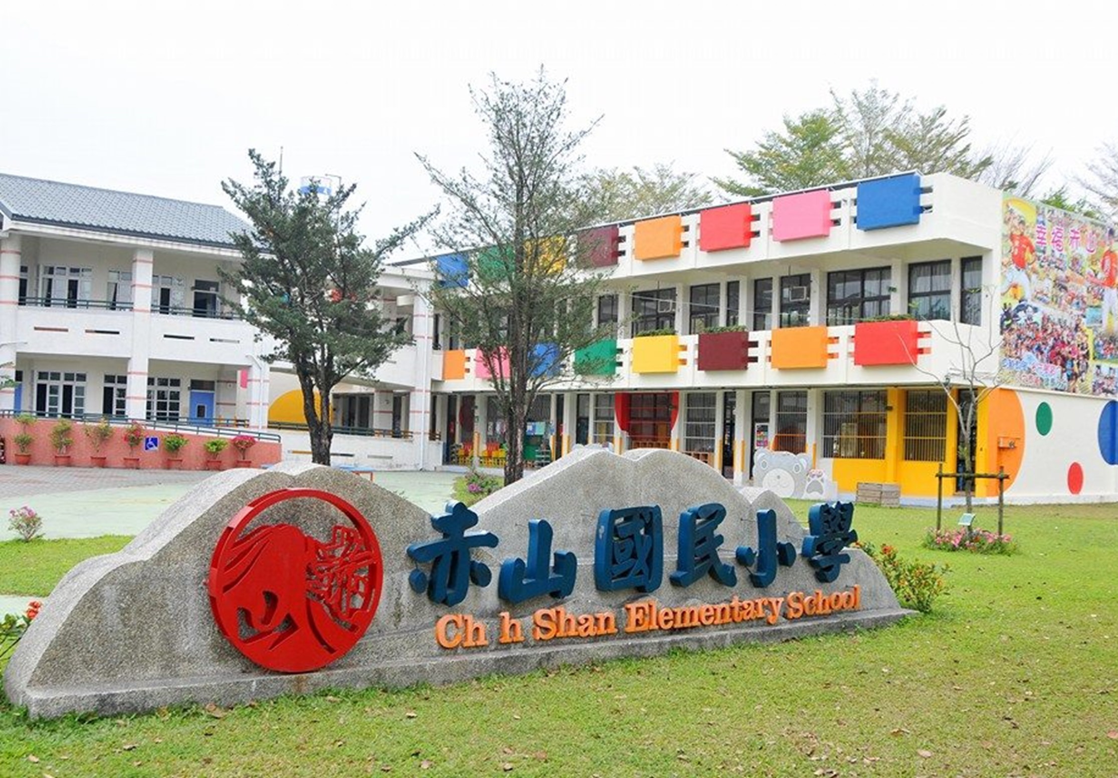 赤山國民小學校園全景，前方草地上放置校名石碑，背景為色彩繽紛的教學建築群，包括白色主校舍、多彩方形裝飾藝術牆面，校園綠化良好，充滿活力的兒童教育環境。