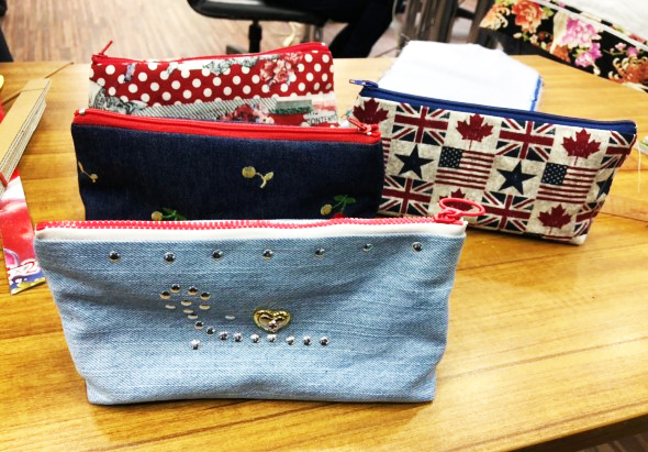 木桌上展示五個手工製作的布料小袋，分別採用紅白圓點、深藍繡花、淺藍珠飾愛心、英式國旗和加拿楓葉等不同圖案設計，展現各式手作創意布藝產品。