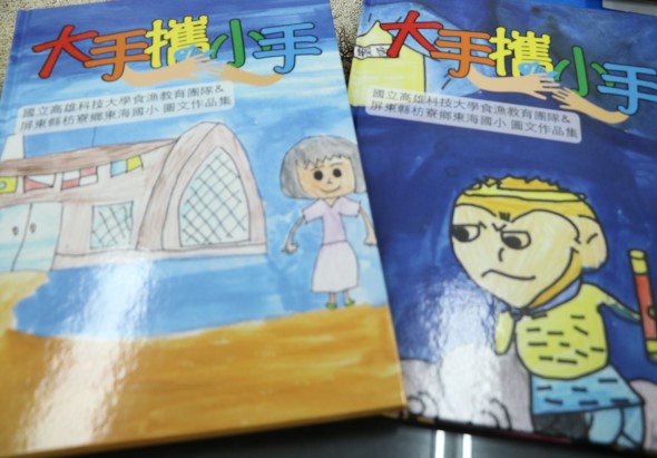 兩本大手牽小手兒童教材書籍並排放置。左冊封面繪有穿著藍色衣服的老年女性人物與建築物；右冊封面繪有黃色衣服的小男孩角色。兩本書均為藍色主調設計，標題採用紅色和綠色文字。