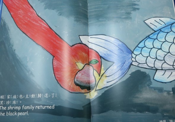 插圖顯示一隻紅色的蝦與兩隻白色的魚相遇。蝦身呈鮮紅色，頭部有黃色區域和綠色眼睛。兩條魚的身體為白色，具有藍色和白色的鱗片紋理。背景為藍綠色水域。圖片下方標有英文文字「The shrimp family returned the black pearl」，以及中文標題提及蝦家族歸還黑珍珠的故事。