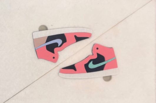 兩雙紅黑配色的Air Jordan 1高筒籃球鞋紙製模型，放置在米色背景上，展示側面和三角形設計細節，具有標誌性的Swoosh標誌。