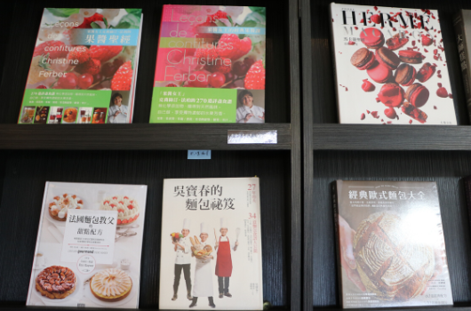 書架上展示六本食譜書籍。上排三本以草莓為主題，包含英文和中文標題的烹飪指南。下排三本為中文食譜，涵蓋甜點製作、服飾搭配和烘焙技巧等主題。書籍排列整齐，展示各式美食和生活相關內容。