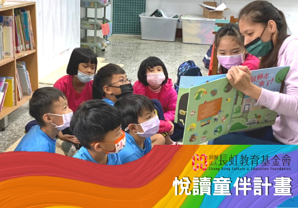 一位老師在教室內向坐成一圈的小學生們講述繪本故事。學生們戴著口罩專注聆聽，老師舉著彩色繪本展示給大家。背景可見書架、黑板和教室物品。下方為「長虹教育基金會」標誌和「悅讀童伴計畫」文字。