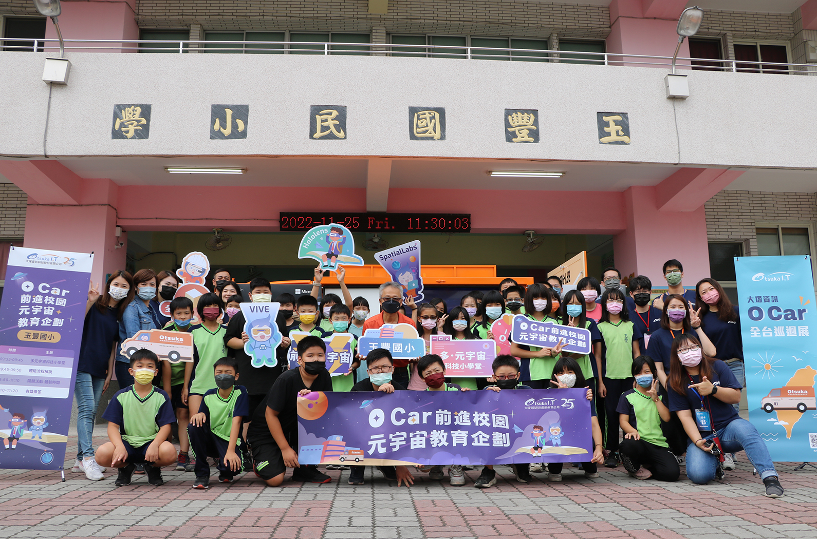 玉豐國小前廣場舉辦「Car前進校園元宇宙教育企劃」活動。大批穿著綠色背心的學生和教職員工聚集合影，手持宣傳標語和卡通角色布景。背景為校舍建築，顯示時間為2022年12月25日上午11時30分。