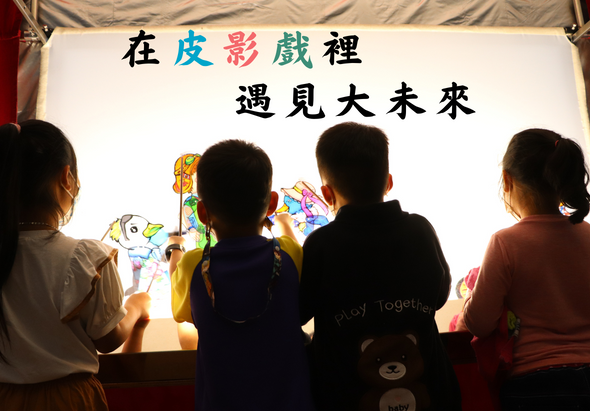 四名兒童面對著一個白色投影幕，幕上展示彩色皮影戲人物，上方寫著「在皮影戲裡遇見大未來」的繁體中文字樣。孩子們正在觀看和互動皮影戲表演。