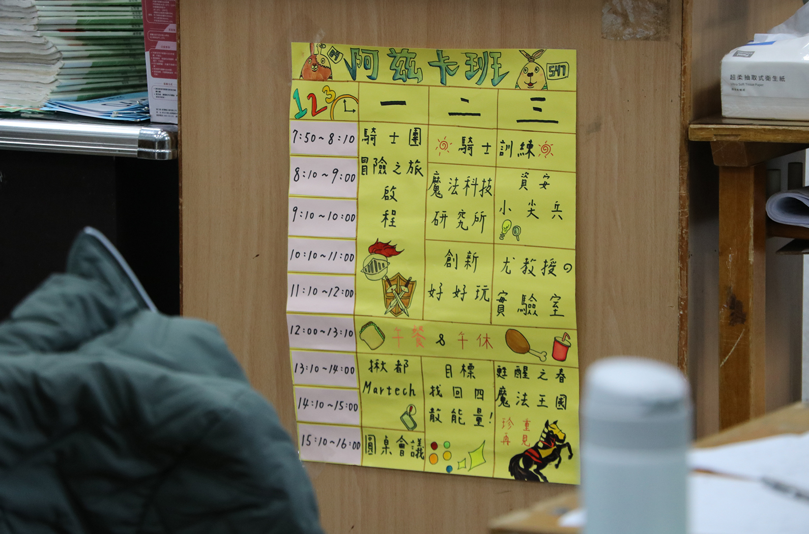 阿純卡班課表，黃色背景，列出每日一至三年級的時程安排。時間從早上7:50至下午3:50，包含課程、活動與休息時間。右側標註各時段的課程名稱，如騎士團、冒險之旅、魔法科技等，並搭配卡通插圖裝飾。