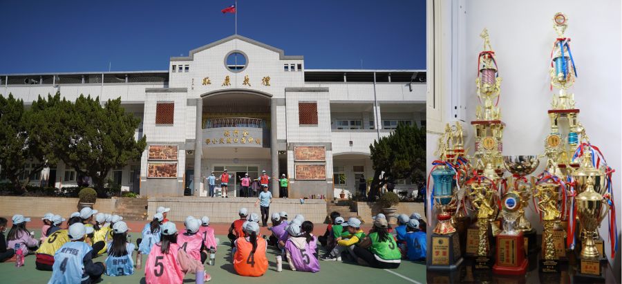 學校操場上，穿著彩色運動服的學生們坐成一圈，面向白色校舍建築。右側展示兩座金色宗教雕像。左側校舍掛著紅旗和宣傳海報，舉辦校園活動或慶典儀式。