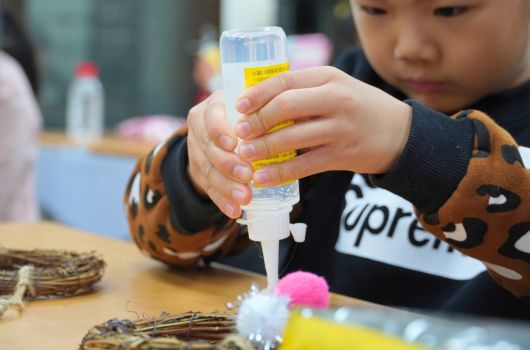 小朋友在手工藝課堂上用膠水進行創意製作，桌上擺放著彩色毛球、樹枝等裝飾材料，正專注地進行美勞活動。