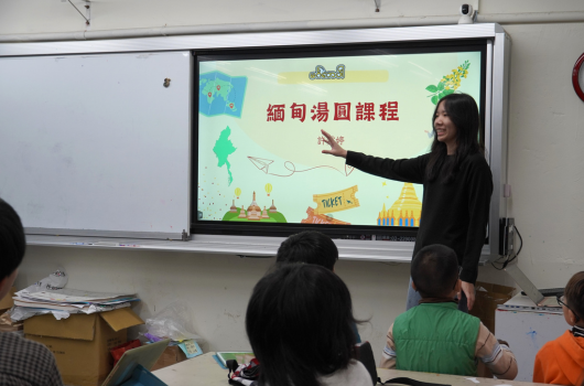 教室內，一位女性教師在互動式電子屏幕前授課，屏幕上顯示「細句澳門課程」標題及卡通插圖。數名學生坐在前排認真聽講。教室左側有白板，右側放置教學用品。