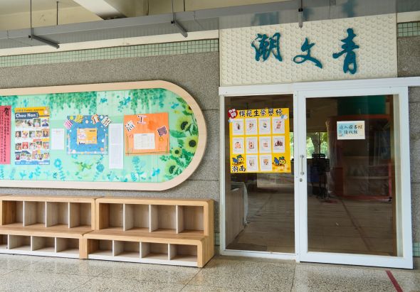 校園走廊展示區，牆上懸掛青湖生青的中文標牌。左側有圓角公布欄展示多彩學生作品和通知。下方木製儲物櫃共十六格。右側為教室入口，玻璃門上貼有黃色班級資訊標籤。整體環境整潔明亮，充滿學校氛圍。