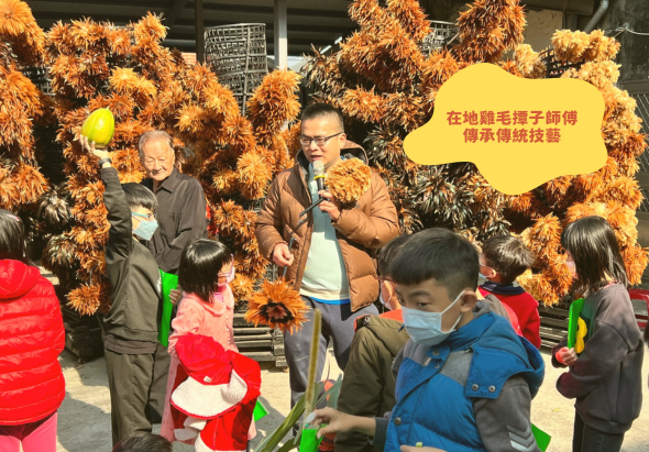 戶外活動現場，兩位長者在掛滿金黃色稻草裝飾的舞台上，向圍成一圈的兒童介紹傳統稻草編織技藝。黃色標語牌寫著「在地農民手工傳承傳統技藝」。兒童穿著紅色和藍色外套認真聆聽。