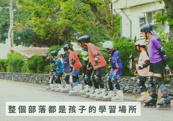 一群穿著橙色和藍色運動服、戴著安全帽的兒童在戶外進行直排輪訓練。他們排成一列，在石板路上練習滑行。背景是綠樹和白色建築。圖片下方文字寫著「整個部落都是孩子的學習場所」。