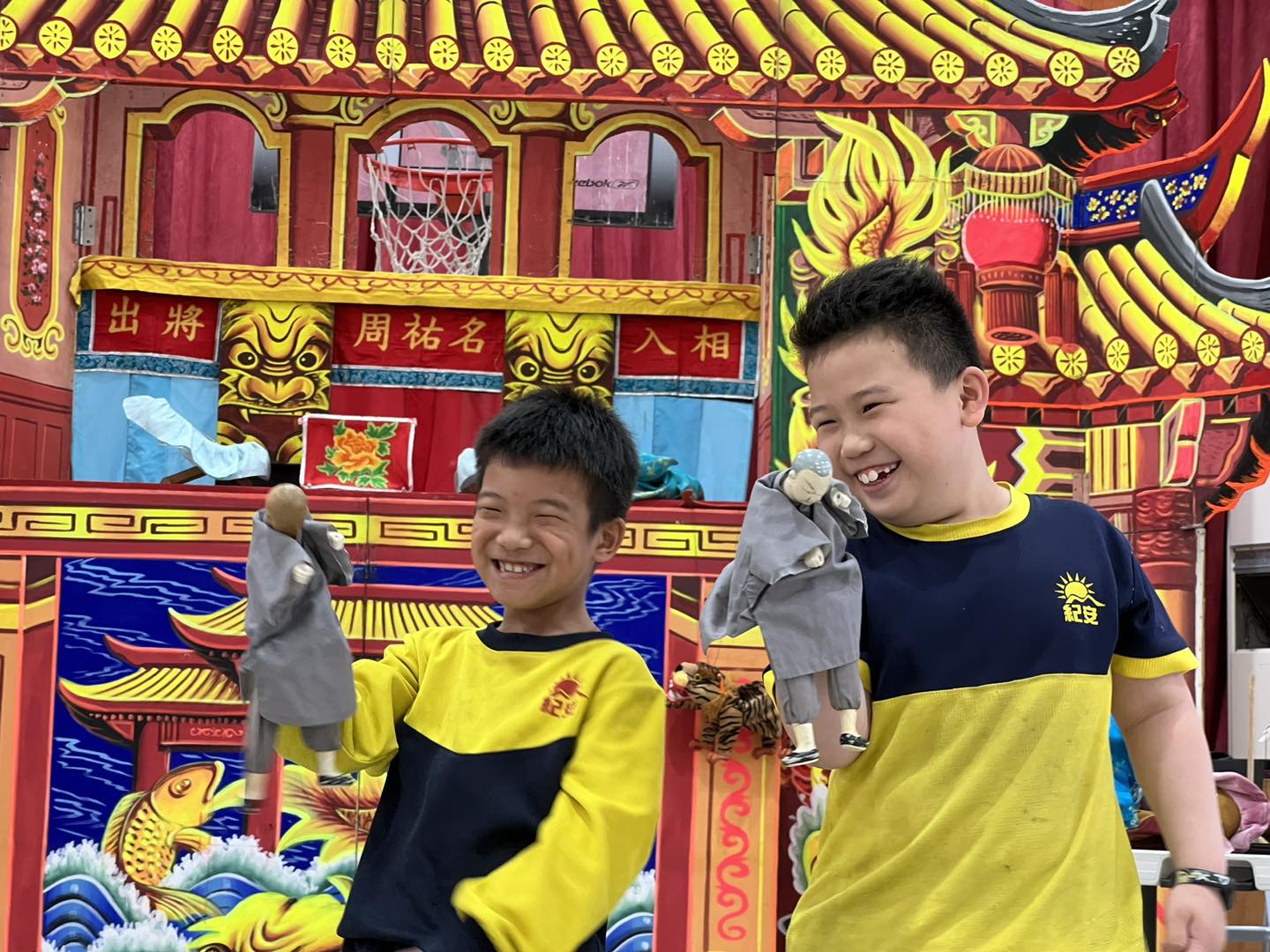 兩名穿著黃黑色運動服的男孩在中式廟宇前合照，背景為紅金色的傳統建築，裝飾有黃色琉璃瓦、龍鳳浮雕和籃球框，兩人都開心地微笑著。