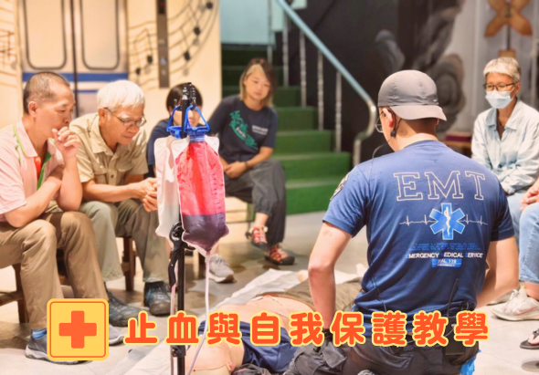 急救員穿著EMT制服，向圍坐的民眾演示止血和自我保護教學。現場有紅十字標誌，多位民眾認真聆聽，展示急救知識推廣活動場景。
