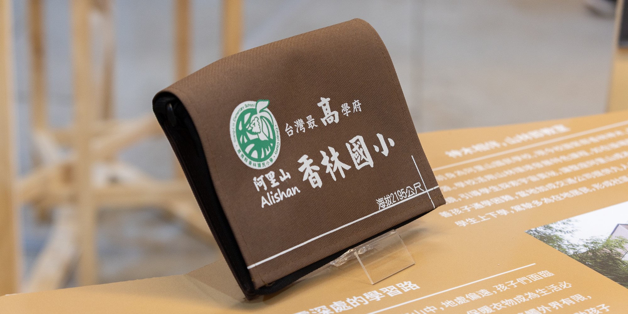 阿里山香林國小名牌立牌，深棕色背景上印有學校logo、校名及台灣最高學府字樣，放置在木製桌面上，背景為室內環境。