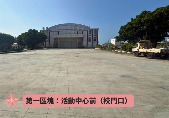 寬敞的廣場前方，一座現代化的紅白相間圓形建築矗立，為活動中心。廣場鋪有整齊的地磚，右側停放貨車。周圍綠樹環繞，晴朗天空。標示牌指示第一區塊位於活動中心前校門口。