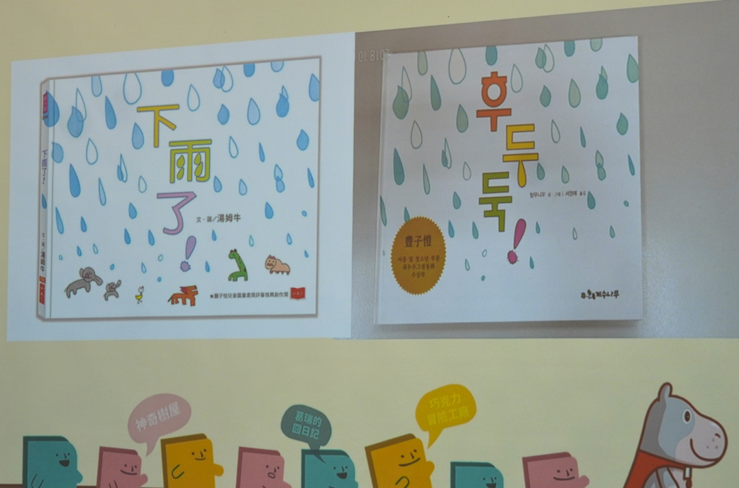 兩本兒童繪本展示，左冊《下雨了》以藍色雨滴為主題，右冊《下雨天》獲得獎項認可。下方展示彩色卡通人物與河馬角色進行對話互動的場景。