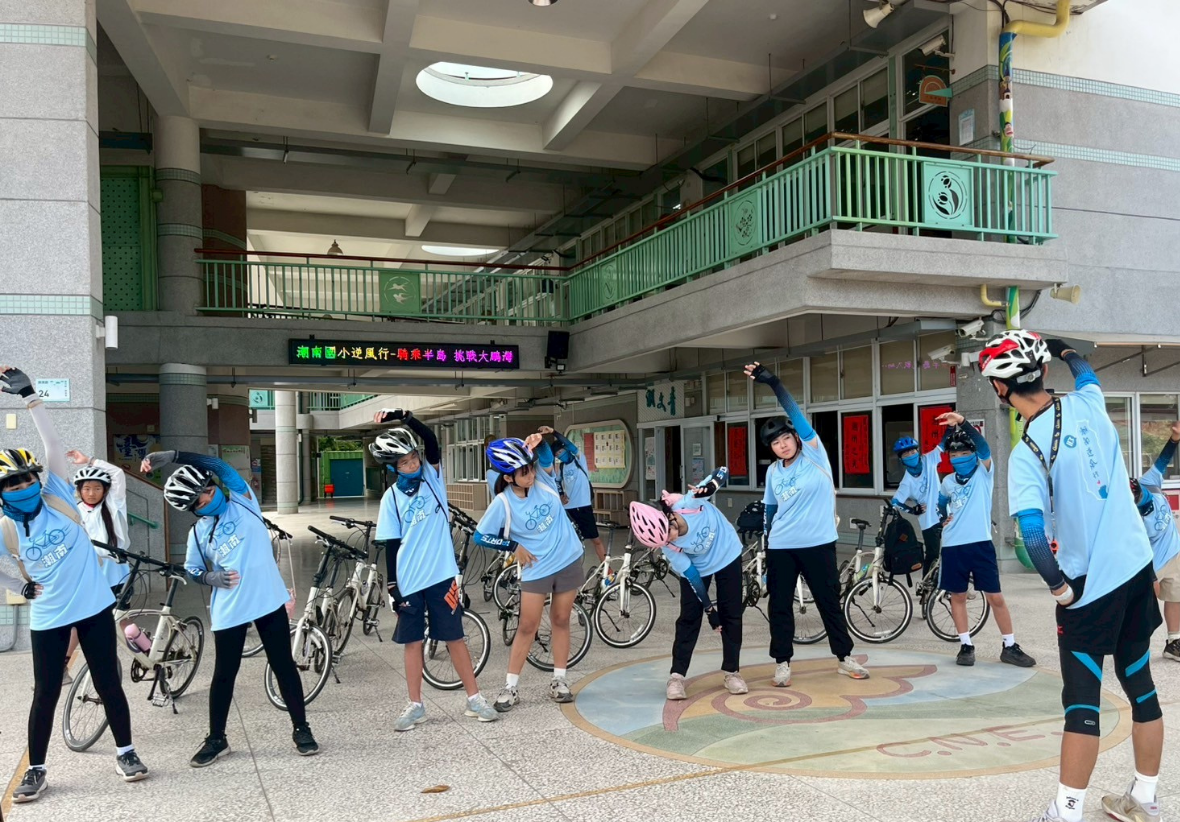 圖片為潮南國小的學生在單車逆風行挑戰前，將單車擺放於後方，穿著藍色衣服及黑色褲子，頭頂上戴著單車帽子，正在進行暖身的畫面 !