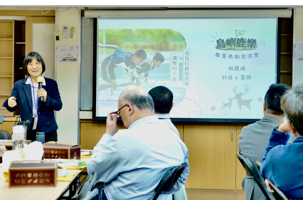 講者於教室前方手持麥克風進行分享，後方投影簡報顯示「島嶼鹿樂 - 教育共創交流會_桃園場_科技 X 藝術」主題，與會者專注聆聽交流。