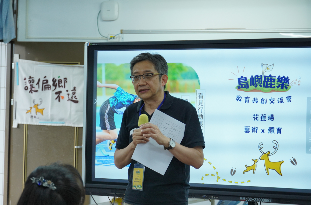 一位男性講者手持講稿與麥克風，在螢幕前致詞。背景投影幕顯示「島嶼鹿樂 - 教育共創交流會_花蓮場_藝術 X 體育」字樣，左側懸掛著「讓偏鄉不遠」的布條。
