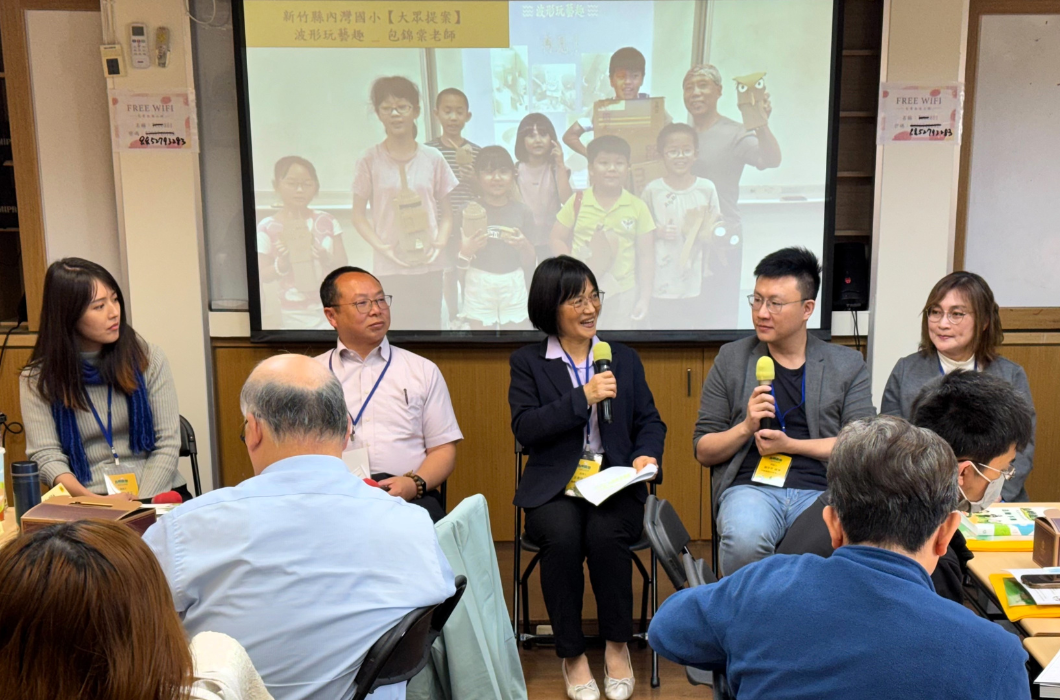 多位與談人於教室內進行教育交流分享，手持麥克風互動討論，後方投影學童活動照片，與會者專注聆聽。