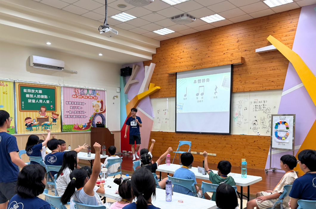 講師在台上利用投影幕講解「身體節奏」課程，台下學生坐在桌前紛紛舉手回應，營造出專注且熱絡的學習氛圍。