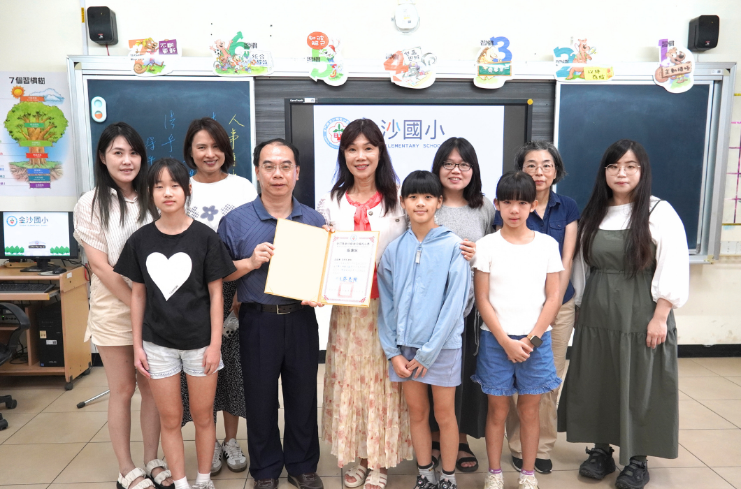 教室電子白板前的大合照，師生與工作人員一字排開，中央由男性代表與老師共同捧著感謝狀，現場氣氛溫馨和諧。