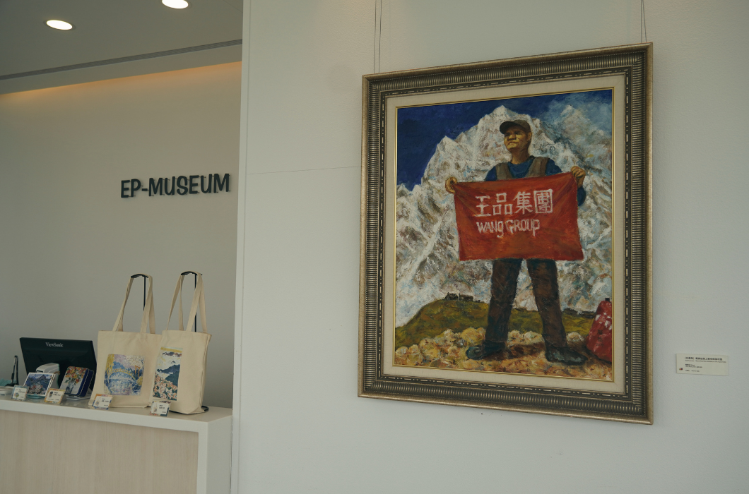 美術館大廳：白色牆面上掛著戴帽人持紅布（寫有『王品集團 Wang Group』）為戴勝益創辦人的油畫。