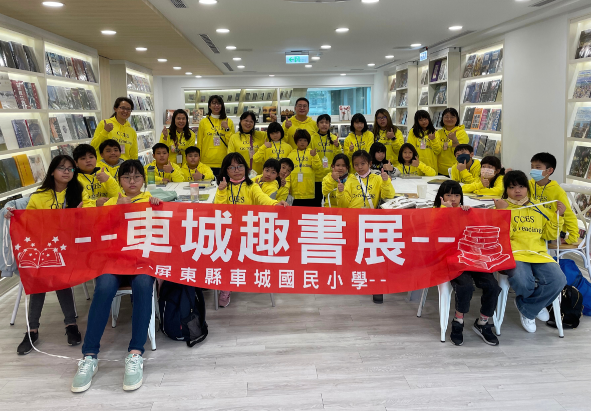 車城趣書展活動現場，屏東縣車城國民小學師生約四十人穿著黃色制服，在圖書館內合影。眾人展示紅色橫幅，上書白色繁體字「車城趣書展」，背景為書架陳列的各類書籍。