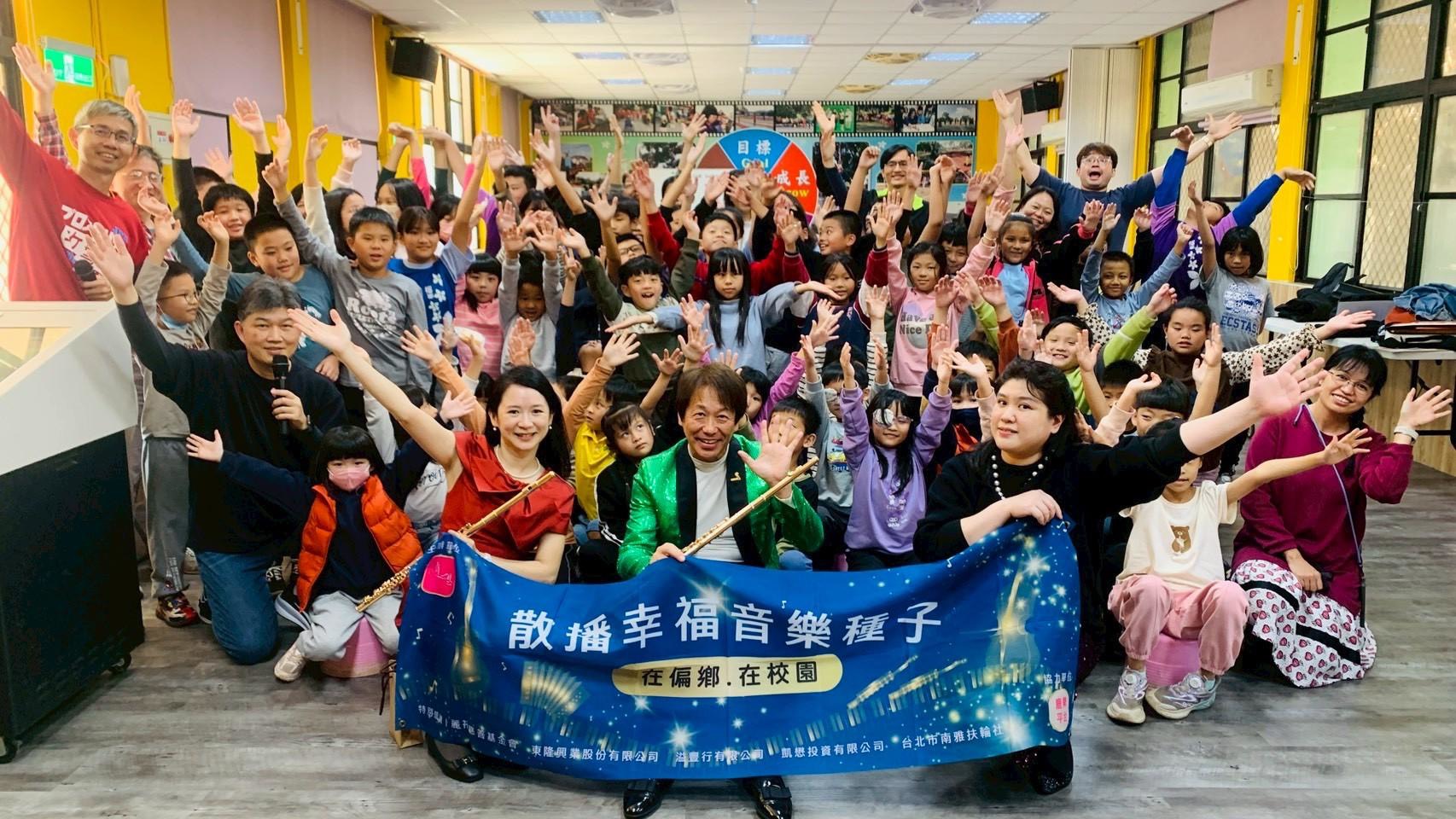 學校教室內，前排中央3位老師舉著寫有「散播幸福音樂種子」的藍色布條，學生們手持獲獎證書，展現音樂教育活動的成果與團隊精神。