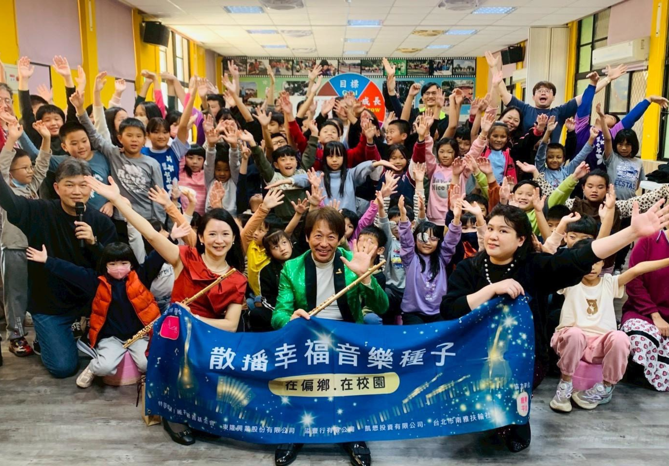 畫面為隨響室內樂演出合照，圖中有三位音樂家，手拉布條。為偏鄉巡演的團體照，畫面中央有音樂家及孩子。