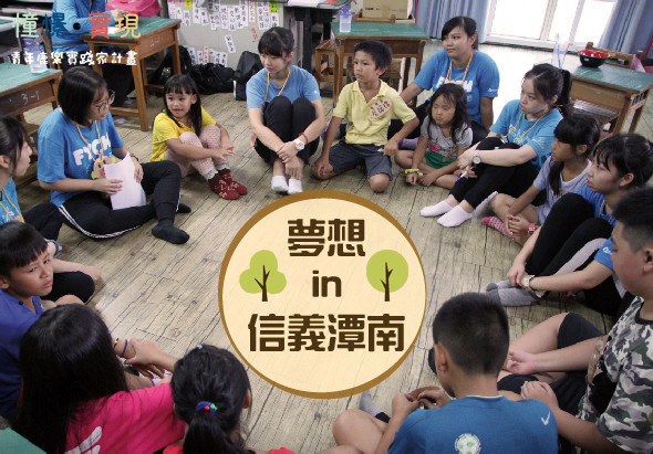 一群兒童穿著藍色和黃色衣服，圍坐在木質地板上參與室內活動。中央有黃色圓形標誌，寫著「夢想in信義漂南」，配有綠色樹木圖案。此為兒童教育或社區服務活動的現場照片。