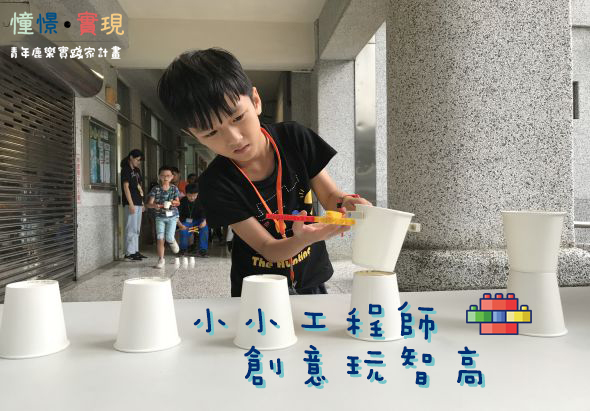 一位年輕講師在室內展示教學活動，面前擺放多個白色杯子，正用木製工具進行互動教學。背景有其他參與者。圖片展示「小小工程師創意玩樂高」主題活動，強調寓教於樂的創意教學方式。