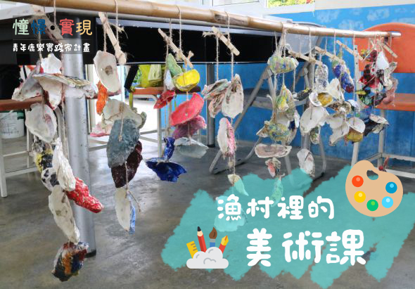 漁村裡的美術課活動現場，展示學生用廢棄漁具和海洋物料製作的五彩繽紛藝術品，掛在繩索上展示。背景有藍紅色建築和調色盤圖案標誌。