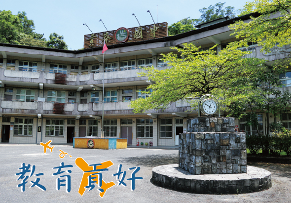 校園廣場中央豎立著一座石製時鐘塔，背景為三層樓校舍建築，懸掛中華民國國旗。下方以黃藍色設計標示校名，象徵教育蓬勃發展。綠樹環繞，呈現寧靜的學校環境。