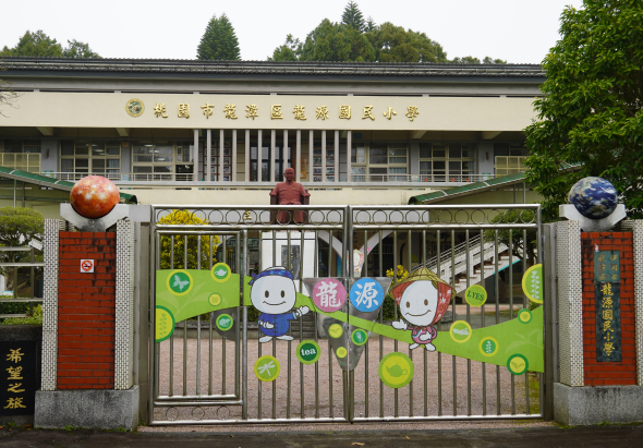 台灣某國民小學校門外觀，門上裝飾著卡通人物和綠色圓形圖案，校舍背後有樹木，展示學校友善溫暖的環境氛圍。