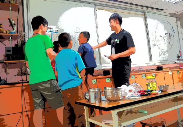 一位教師在課堂上向穿著綠色、藍色和深藍色上衣的三名學生進行科學實驗教學，桌上放著燒杯、玻璃棒等實驗器材，黑板上有教學內容，窗外可見白色建築物。