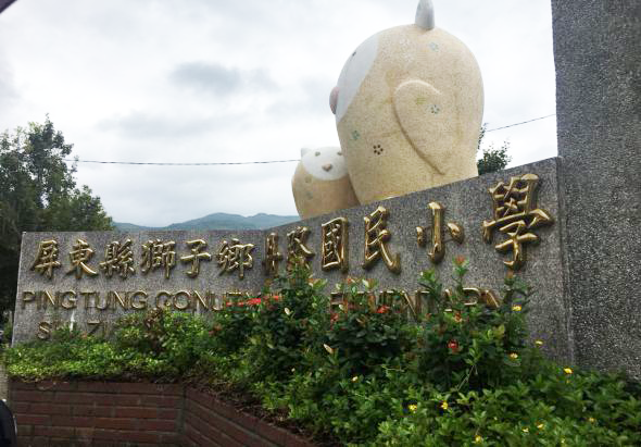 平阳县瑞阳千秋时代国民小学校门石碑，上方有两只石雕大象，碑面刻有中英文校名，周围绿化环境优美，背景为山区景观。