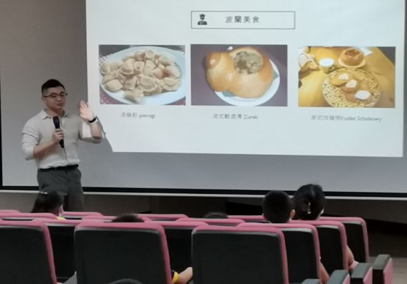 男性講者在演講廳進行簡報，投影幕上展示「品嚐美食」主題，呈現三張食物照片：左為小籠包、中為包子、右為點心。講者手持麥克風，身旁有粉紅色座椅。