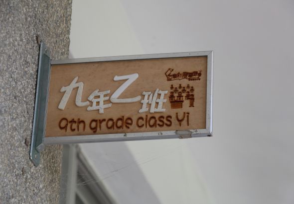 九年乙班教室門牌，以木質背景搭配白色和棕色字體，顯示中文班級名稱及英文「9th grade class VI」，上方裝飾有城堡圖案。